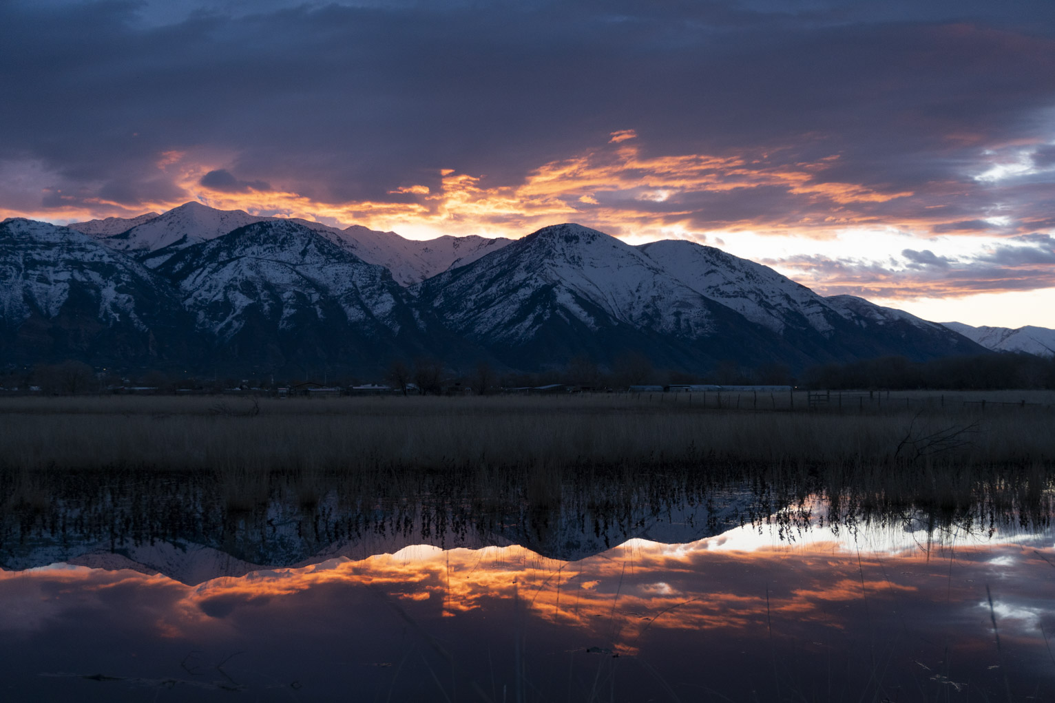 The snowy mountains appear intensely blue under the dramtically lit clouds, their reflection in water below